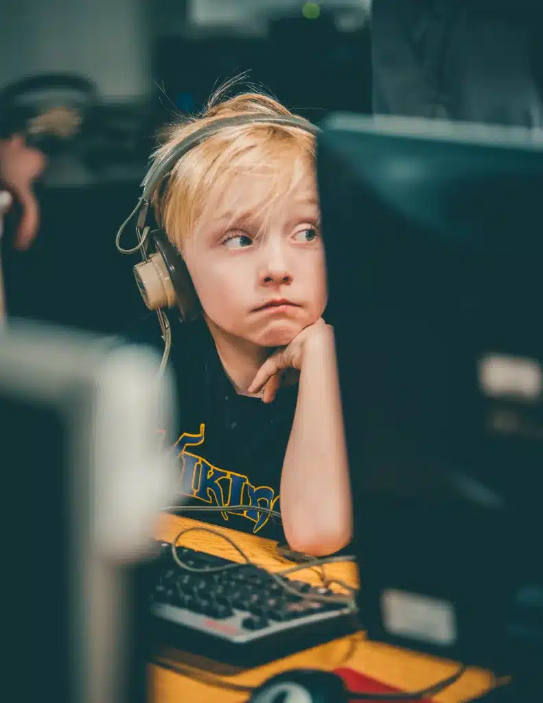 My ADHD Child can behave at school but not at home, why? Image of a child sitting at a computer with headphones on, looking away from the screen. 