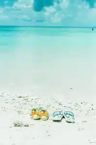 Two pairs of sandals on a very white sandy beach. Summer vacation with ADHD