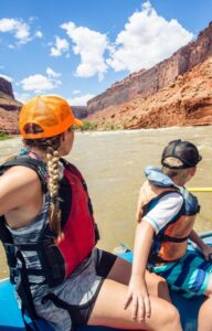 A family, including an older sister and younger brother, admiring the vast red valley during their whitewater rafting trip.