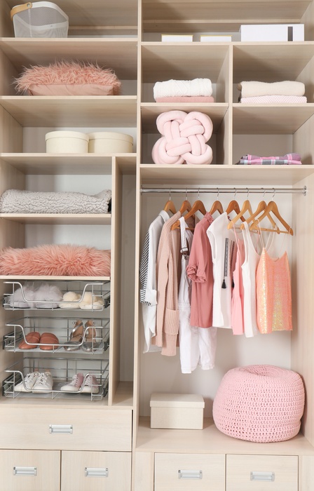 An organized closet contains shelves with folded clothing, tan hangers, shoes, drawers, and rolled-up towels.