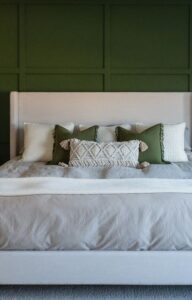 A king-size bed is in a large bedroom against a green wall. The bed contains white and green pillows.