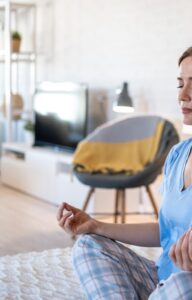 A young woman meditating on her bed in pajamas in a studio apartment, and finding inner peace at home.