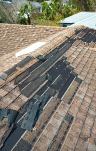 A close-up of a roof with major damage, large chunks of shingles torn from the roof and missing.