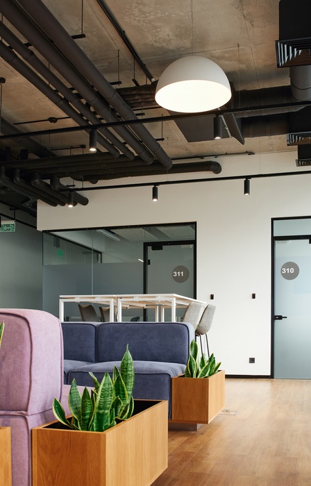 An office with various types of seating, including chairs at a high-top table and colorful couches. Plants are also around the room.