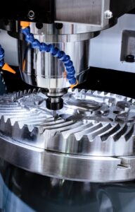 A CNC machine working on a ridged, circular piece of metal. The metal is held in place just below the machine's tip.