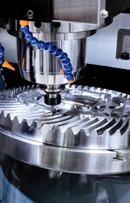 A CNC machine working on a ridged, circular piece of metal. The metal is held in place just below the machine's tip.