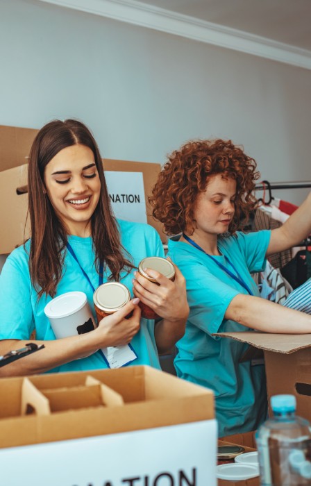 Four individuals wearing matching blue shirts sort through boxes of supplies at a table while taking notes on a clipboard.