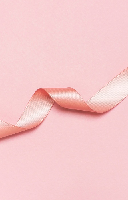 A pastel pink satin ribbon is gently twisted and lying on a solid pink background. The light reflects off the ribbon.