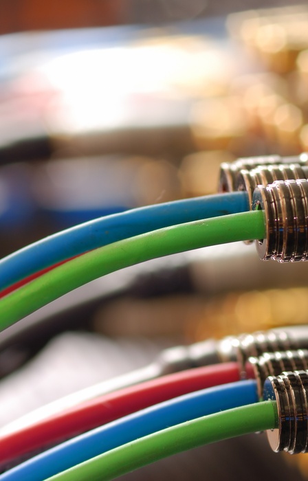 A close-up of red, blue, and green cables plugged into audio ports on equipment, with metallic connectors in focus.