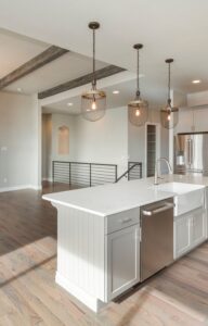 An open concept farmhouse style home with a kitchen island dividing the primary living room space and three pendant lights.