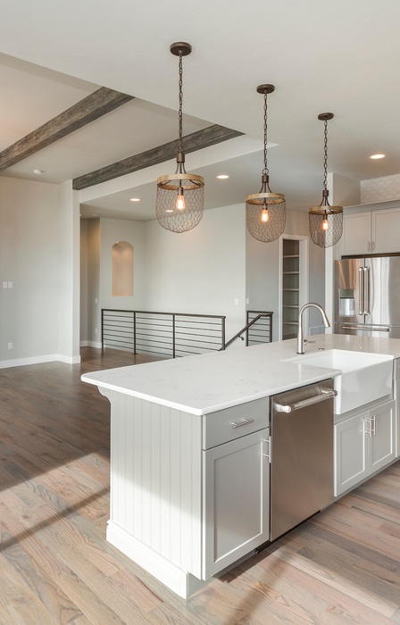 An open concept farmhouse style home with a kitchen island dividing the primary living room space and three pendant lights.