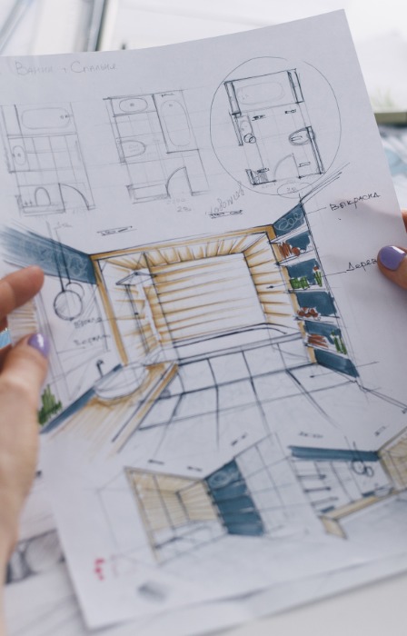 A point-of-view shot of a person with purple fingernails holding sketches and floor plans for a home bathroom.