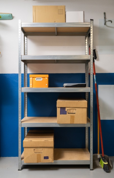 A five-level metal shelving unit contains cardboard boxes of various sizes. It sits against a blue and white wall.