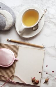 Cozy self-care essentials, including slippers, herbal tea, a sleep mask, and a journal on a marble surface.