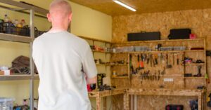 A person stands in a well-organized workshop, facing a workbench lined with neatly arranged tools and equipment.