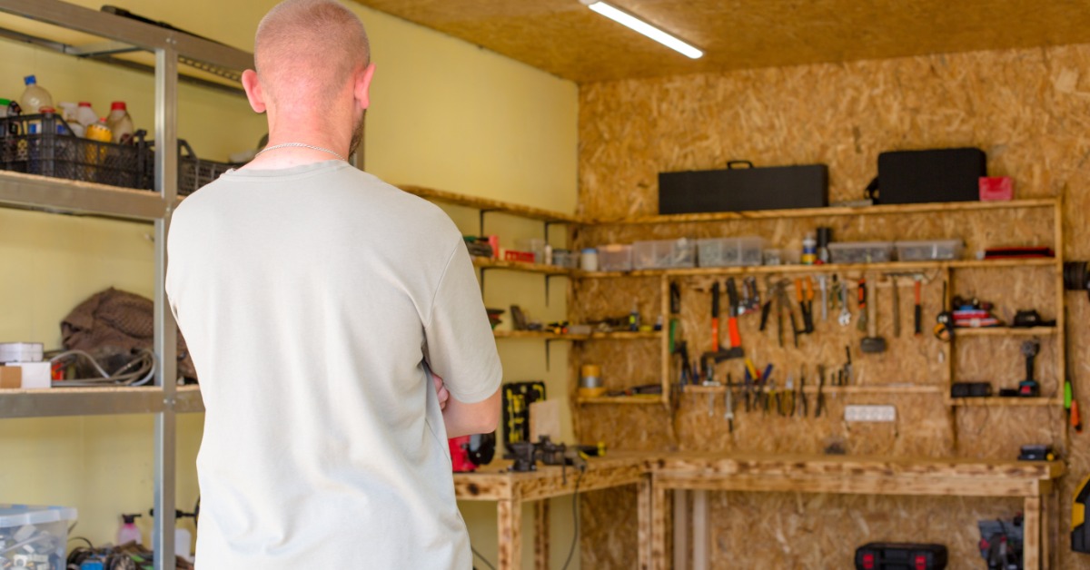 A person stands in a well-organized workshop, facing a workbench lined with neatly arranged tools and equipment.