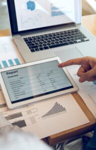 A tablet showing a financial report as two people review charts and handwritten notes next to a laptop.