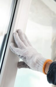 A person wearing gloves and a long sleeve shirt is pushing a window pane into place. There is a white wall next to the window.