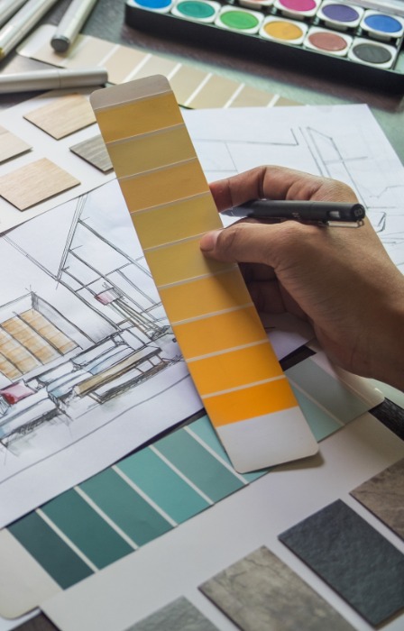 A person is holding up a slip of color splotches. There are papers and a diagram on a desk.
