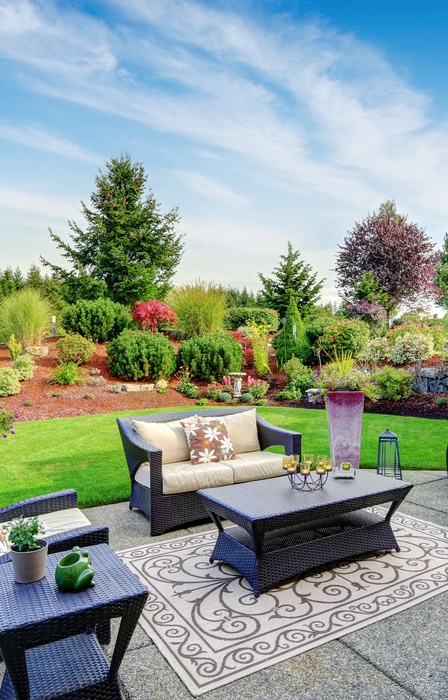 A backyard patio area with a few nice patio chairs set up with cushions and pillows. There's a coffee table.